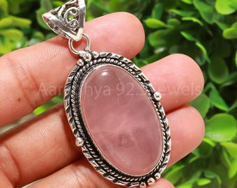 May include: A silver pendant with an oval rose quartz gemstone. The pendant has a decorative silver border and a detailed bail. The text "Aaranya 92. jewels" is visible on the pendant.