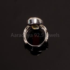 May include: A silver ring featuring a large, oval, pale-green gemstone. The ring has an intricate band design. The text "Aaradhya 92.5 jewels" is visible.