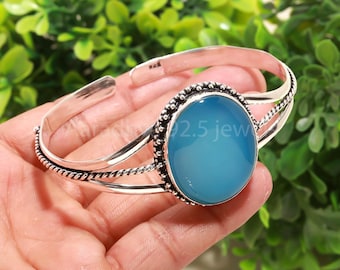 May include: A silver cuff bracelet featuring a large, oval, light blue gemstone. The gemstone is framed by a beaded border. The bracelet has a simple, elegant design, suitable for daily wear. The text "92.5 jew" is visible on the gemstone.