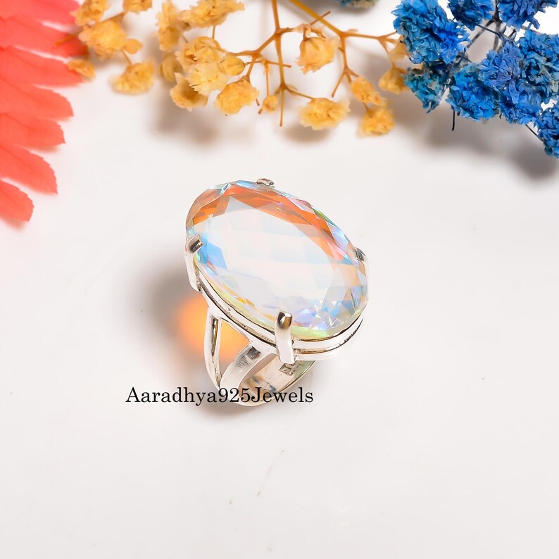 May include: A silver ring featuring a large, oval-cut gemstone with iridescent colors. The gemstone is set in a silver band. The text "Aaradhya925Jewels" is printed on the ring.