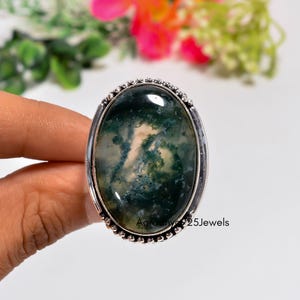 May include: An oval moss agate ring set in a polished silver band with a beaded edge. The gemstone features translucent white and green inclusions resembling mossy patterns. The text Aaranya925Jewels is visible on the lower right side.