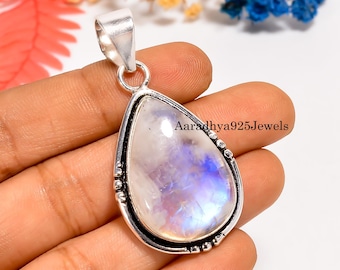 Pode incluir: Pingente em forma de gota com uma grande pedra da lua iridescente. A pedra é engastada em metal prateado com uma borda decorativa. O pingente tem uma argola na parte superior para uma corrente. O texto "Aaradhya925Jewels" é visível.