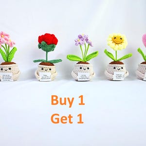 Puede incluir: Cinco macetas de flores de ganchillo con caras sonrientes, cada una con una flor diferente: rosa, roja, morada, amarilla y un corazón rosa. Cada maceta tiene un pequeño letrero con un mensaje positivo. Las flores están sobre un fondo blanco.
