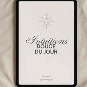 Könnte beinhalten: Ein schwarzes Tablet zeigt die Worte "Intuitions Douce Du Jour" in einer stilvollen Schriftart, darüber eine Sonne. Der Text "Une création de @rituelenpoche" befindet sich unten. Das Tablet liegt auf einem beigen Hintergrund.