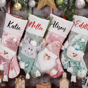 Op de afbeelding: Vier kerstsokken met de namen Katie, Nellie, Alison en Edith. Elke sok heeft een ander ontwerp, met een sneeuwpop, rendier en kerstman. Ze hangen met kerstversieringen.