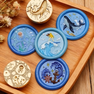May include: A selection of decorative wax seal stamps with marine designs. The stamps depict a whale, a surfer, a jellyfish, and an anchor. The stamps are in gold and blue hues, ideal for adding a nautical theme to crafts and stationery.