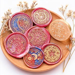 Op de afbeelding: Een verzameling decoratieve waszegels met hemelse ontwerpen, waaronder manen, sterren en geometrische patronen. De zegels zijn in rood, blauw en goud, gerangschikt op een houten bord.