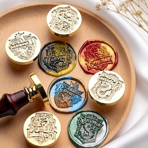 May include: A collection of circular metal wax seal stamps and finished wax seals featuring the four Hogwarts house crests: Gryffindor, Hufflepuff, Ravenclaw, and Slytherin. The set includes a wooden handle attached to a gold-toned metal stamp head.