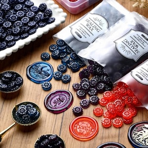 Peut inclure: Un assortiment de perles de cire à cacheter de différentes couleurs, dont bleu, rouge et violet, ainsi que des sceaux de cire avec différents motifs. L'image présente également des cuillères à fondre la cire et des contenants de perles de cire.