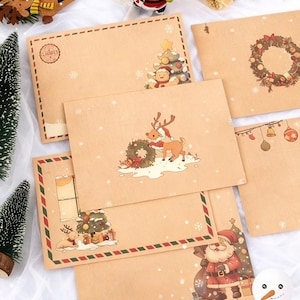 May include: A selection of Christmas-themed envelopes. The tan envelopes feature festive illustrations such as Santa Claus, reindeer, Christmas trees, and wreaths. Snowflakes are scattered across the envelopes, and some have decorative red and green borders.