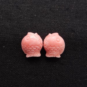 Pode incluir: Duas contas de coral rosa em forma de peixe. As contas são esculpidas com escamas e têm um design detalhado.