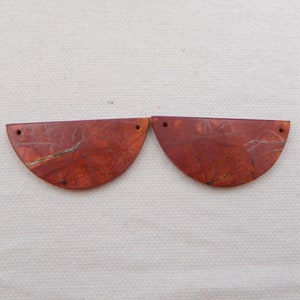 Puede incluir: Dos cuentas de piedra de forma semicircular de color rojo y marr&oacute;n con agujeros perforados.