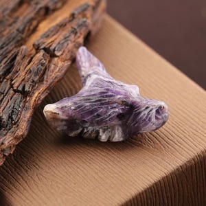 May include: A carved purple and white stone figurine shaped like a wolf head. The mineral features deep violet hues mixed with white streaks and intricate etched details representing the animal's snout, ears, and fur texture in a polished finish.