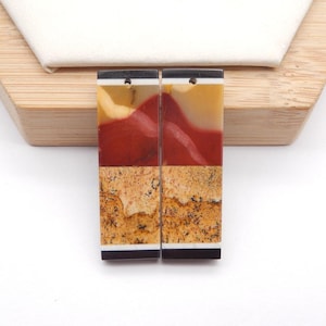 May include: Two rectangular earrings with a layered design. The top section is a mix of yellow and cream, followed by a red section, and a textured tan and brown section at the bottom. The earrings have black and white accents.