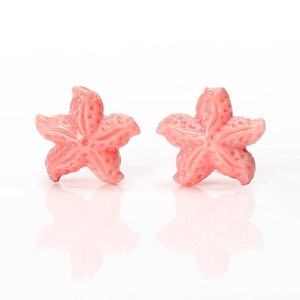 Peut inclure: Une paire de boucles d'oreilles en forme d'étoile de mer rose. Les boucles d'oreilles sont en matériau lisse et brillant et ont un aspect délicat et féminin.