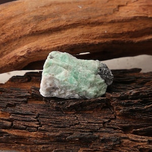 Peut inclure: Un spécimen minéral brut et non poli présentant une structure cristalline vert menthe pâle avec des inclusions blanches et gris foncé. La pierre a une forme irrégulière et dentelée avec une surface rugueuse et texturée.