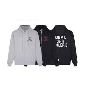 May include: Three zip-up hoodies in gray, black, and dark gray. Each hoodie has a hood and the text "DEPT. de la GALERIE" or "CEPT. le la GALERIE" printed on the front or back. The hoodies are displayed against a white background.