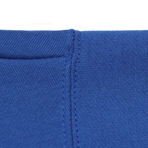 May include: Close-up of a royal blue garment, possibly a t-shirt or sweatshirt, showing the neckline and a vertical seam. The fabric appears to be a soft knit material. The stitching is visible and detailed.