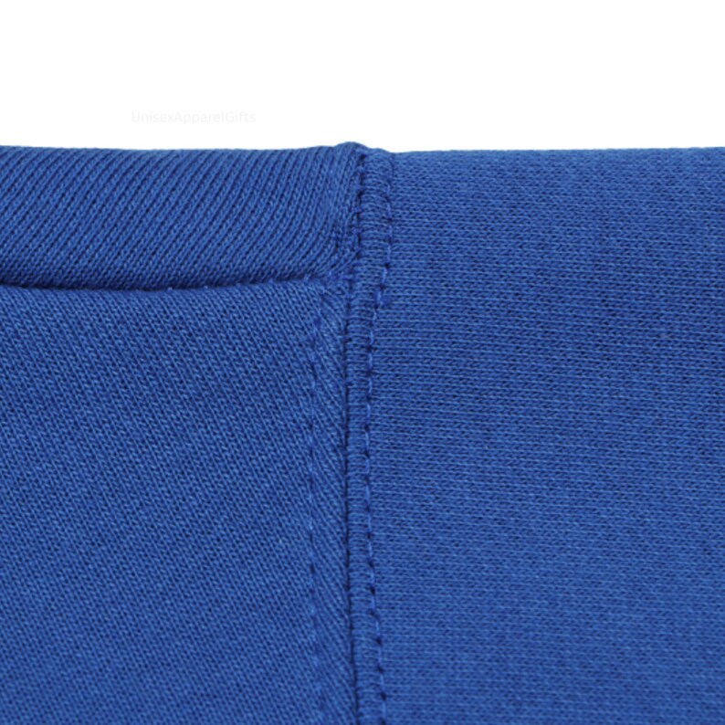 May include: Close-up of a royal blue garment, possibly a t-shirt or sweatshirt, showing the neckline and a vertical seam. The fabric appears to be a soft knit material. The stitching is visible and detailed.