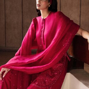 K&ouml;nnte beinhalten: Ein magenta-farbenes Ensemble mit einer lang&auml;rmeligen Tunika mit Perlenverschluss und passender Hose. Das Outfit beinhaltet einen flie&szlig;enden Schal und ein Stirnband. Die Hose hat gestickte Details.