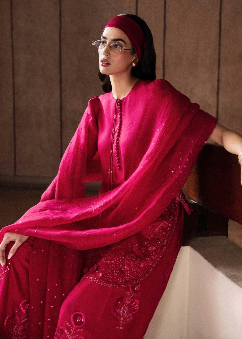 K&ouml;nnte beinhalten: Ein magenta-farbenes Ensemble mit einer lang&auml;rmeligen Tunika mit Perlenverschluss und passender Hose. Das Outfit beinhaltet einen flie&szlig;enden Schal und ein Stirnband. Die Hose hat gestickte Details.