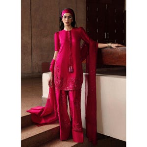 K&ouml;nnte beinhalten: Ein leuchtend fuchsiafarbenes Ensemble mit einer kurz&auml;rmeligen Tunika mit aufwendiger Stickerei und passenden weiten Hosen. Das Outfit beinhaltet einen langen Schal und ein Stirnband. Die Tunika hat eine Knopfleiste und einen Quastenbesatz. Ein mutiges Mode-Statement.
