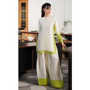 May include: A two-piece outfit featuring a long-sleeved tunic and wide-leg pants. The tunic is white with a row of buttons down the front and lime green accents on the sides and sleeves. The pants are white with lime green trim at the hem.