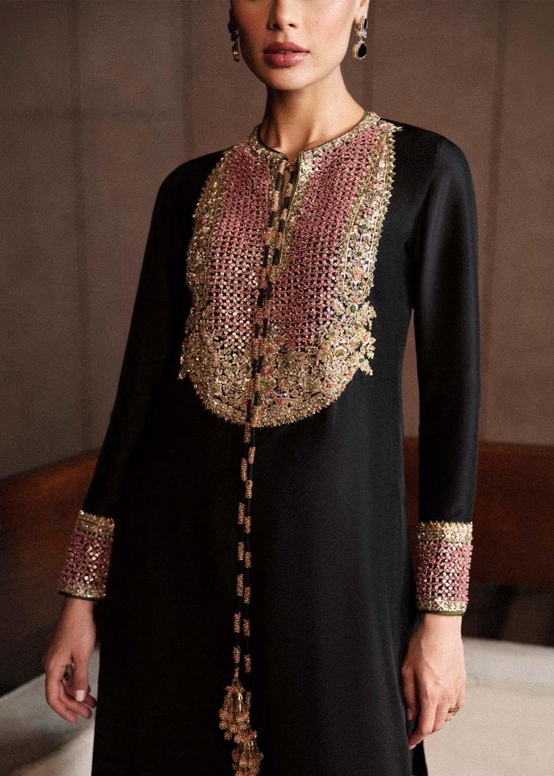 K&ouml;nnte beinhalten: Schwarzes Langarmkleid mit aufwendiger rosa-goldener Stickerei am Ausschnitt und an den Manschetten. Das Kleid hat eine zarte Perlenverzierung auf der Vorderseite, die dem Design einen Hauch von Eleganz verleiht.