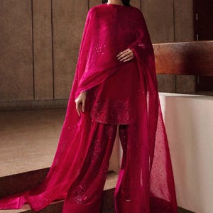 K&ouml;nnte beinhalten: Ein lebendiges fuchsiafarbenes Ensemble mit Tunika, weiten Hosen und einem flie&szlig;enden Schal. Das Outfit ist mit dezenten Pailletten verziert, und ein passendes Stirnband vervollst&auml;ndigt den Look. Geeignet f&uuml;r besondere Anl&auml;sse.