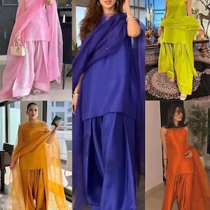 K&ouml;nnte beinhalten: Eine Auswahl an farbenfrohen Salwar-Kameez-Outfits. Jedes Outfit besteht aus einem Oberteil, einer weiten Hose und einem transparenten Schal. Die Farben sind Rosa, Blau, Gelb, Gr&uuml;n und Orange. Die Kleidung ist aus einem gl&auml;nzenden, seidigen Stoff gefertigt.