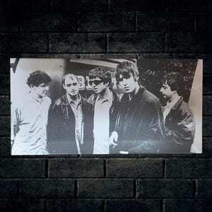 May include: Monochrome photograph of a five-member band. The image is a portrait of the band, with the members standing close together. The image is set against a black brick wall.