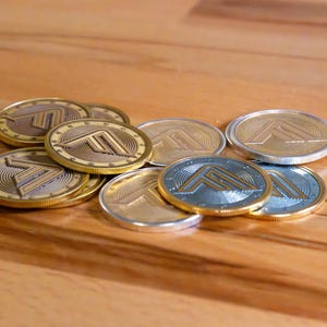 May include: A collection of circular metal coins featuring a stylized letter F logo embossed in the center. The coins have a two-tone design with gold-colored rims and alternating silver or gold-colored centers, each surrounded by a ring of small stars.