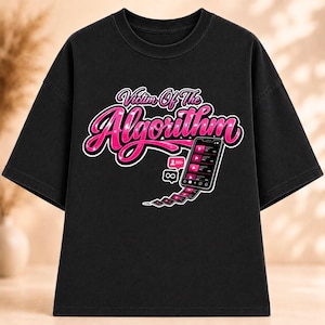 Puede incluir: Una camiseta negra de manga corta con el texto "Victim Of The Algorithm" en una fuente cursiva de color rosa intenso. Debajo del texto hay un gráfico de un teléfono inteligente que muestra un feed de video con un icono de notificación y una estela de miniaturas de video.