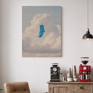 Può includere: Stampa su tela raffigurante un calzino blu appeso a un filo per il bucato su uno sfondo di soffici nuvole bianche. L'opera d'arte ha un aspetto morbido e strutturato, che evoca un senso di fantasia e surrealismo. La tavolozza dei colori è dominata da blu e bianchi.