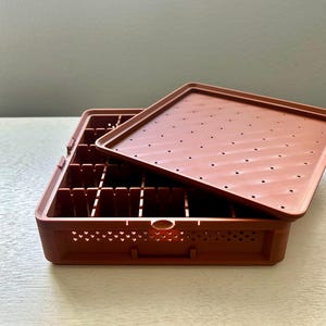 May include: A brown plastic seed starting tray with a matching lid. The tray is divided into multiple small compartments. The lid has small holes for ventilation. The tray is designed for starting seeds indoors.