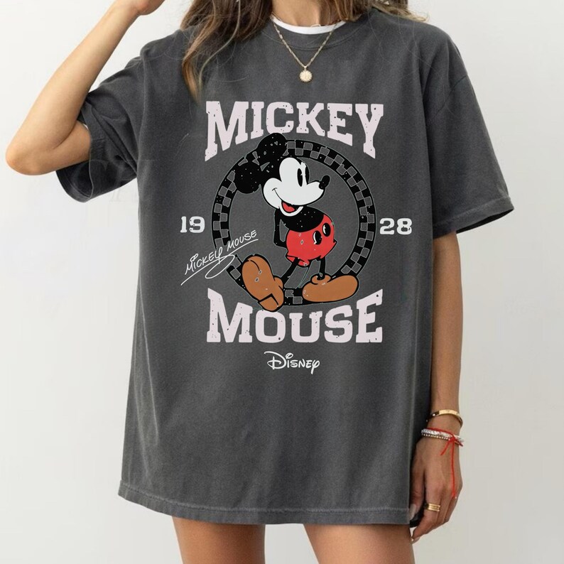 May include: Dark gray t-shirt featuring a classic Mickey Mouse graphic. The design includes the words "Mickey Mouse" and "Disney", along with the year "1928". The shirt has a vintage, distressed look.