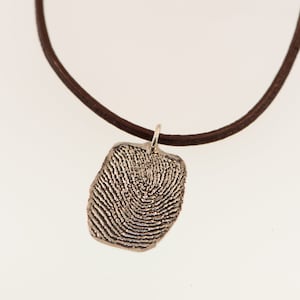 May include: A silver fingerprint pendant necklace on a brown leather cord.