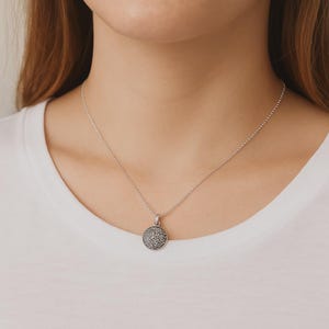 Könnte beinhalten: Eine silberne Kettenkette mit einem runden Anhänger, der mit kleinen, funkelnden Steinen besetzt ist.