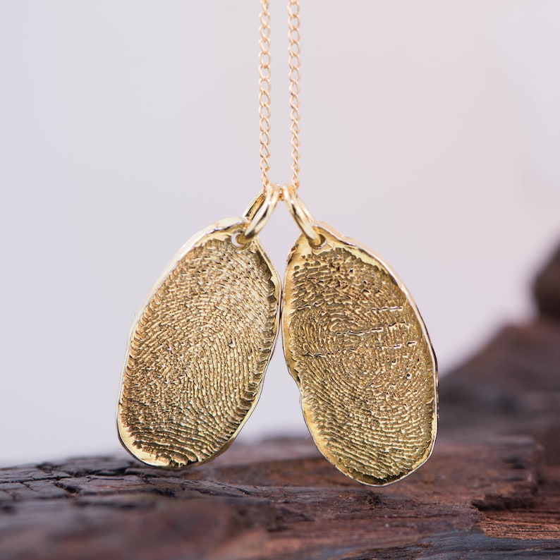 K&ouml;nnte beinhalten: Goldkette mit zwei ovalen Anh&auml;ngern mit detaillierten Fingerabdr&uuml;cken.