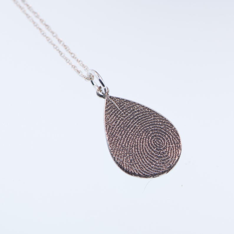 May include: Silver teardrop pendant necklace with a fingerprint design. The pendant is on a silver chain.