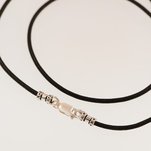May include: A black leather cord necklace with a silver clasp and decorative beads.