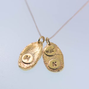 K&ouml;nnte beinhalten: Goldkette mit zwei ovalen Anh&auml;ngern. Ein Anh&auml;nger hat den Buchstaben "M" und der andere den Buchstaben "K" sowie die Worte "My Love".