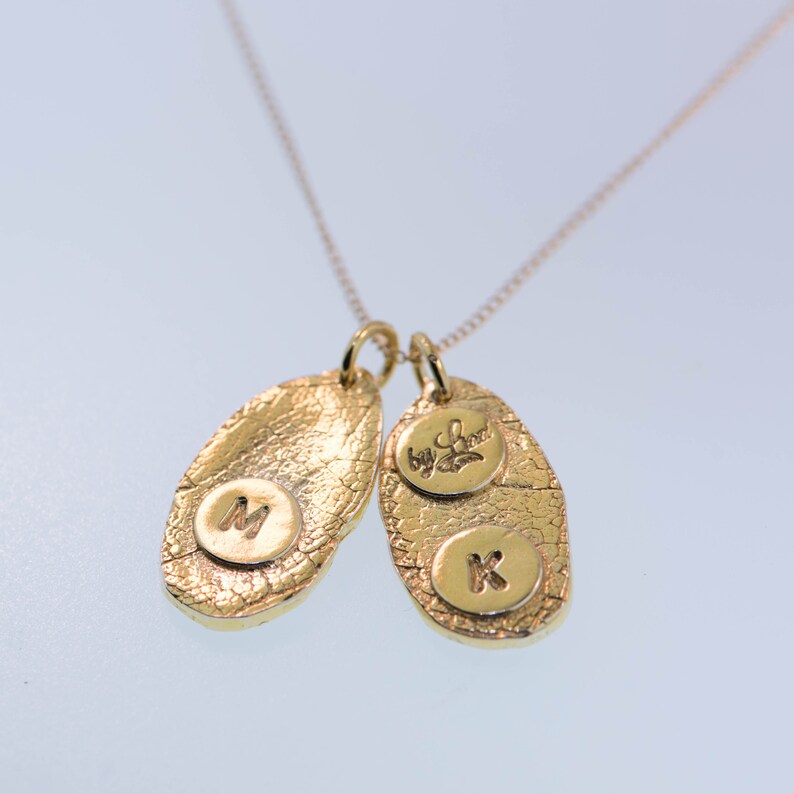 K&ouml;nnte beinhalten: Goldkette mit zwei ovalen Anh&auml;ngern. Ein Anh&auml;nger hat den Buchstaben "M" und der andere den Buchstaben "K" sowie die Worte "My Love".