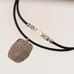 Peut inclure: Un collier avec pendentif empreinte digitale en argent et cordon en cuir noir. Le pendentif rectangulaire pr&eacute;sente des cr&ecirc;tes papillaires d&eacute;taill&eacute;es. Le collier a un fermoir et des perles d&eacute;coratives en argent.