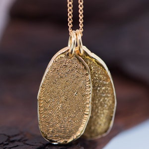 K&ouml;nnte beinhalten: Eine goldene Kettenkette mit zwei ovalen Anh&auml;ngern. Die Anh&auml;nger sind mit einem Fingerabdruckmuster strukturiert.