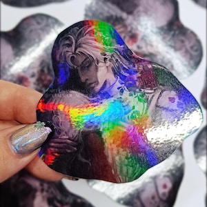 May include: A holographic sticker featuring a detailed illustration of a person with long hair, rendered in shades of gray and black. The sticker has a rainbow-colored, iridescent effect. The text "ART BY NATALIA" and "@PETALS OF AETHER" is visible.