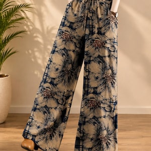 May include: Wide-leg trousers featuring a tan and dark blue plaid pattern overlaid with large, dark floral illustrations. The pants have a high-waisted design with an adjustable drawstring waistband and side pockets, creating a loose, flowing silhouette.
