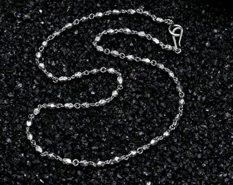 May include: A silver necklace with a delicate chain and faceted beads. The necklace has a hook clasp and is displayed on a dark, textured surface. The chain is approximately 18 inches long.