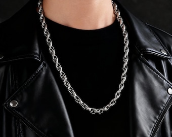 May include: Silver-colored chain necklace with oval links. The necklace is worn over a black shirt and a black leather jacket. The chain is a simple, yet bold accessory.