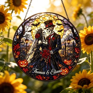 May include: A circular stained glass suncatcher featuring a skeleton couple in formal wedding attire, including a black dress and top hat, surrounded by pumpkins, bats, and a full moon. The text 'Thomas & Eliana' is printed at the bottom.